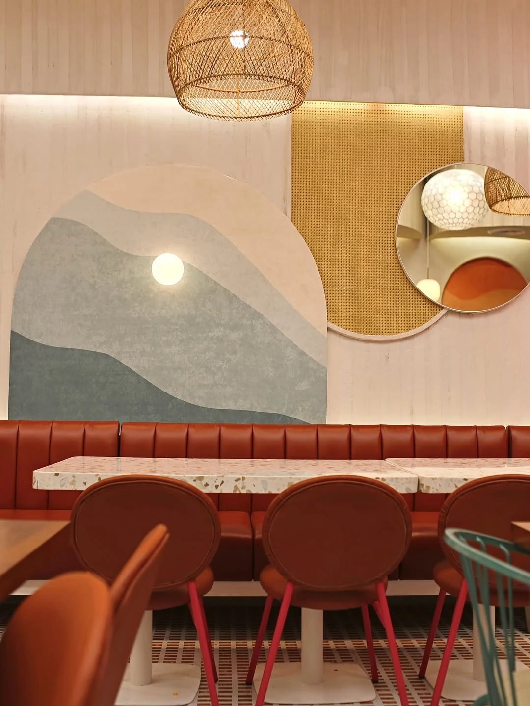 Actual curved rust-colored booth seating, terrazzo tables and rattan pendant at California Steaks